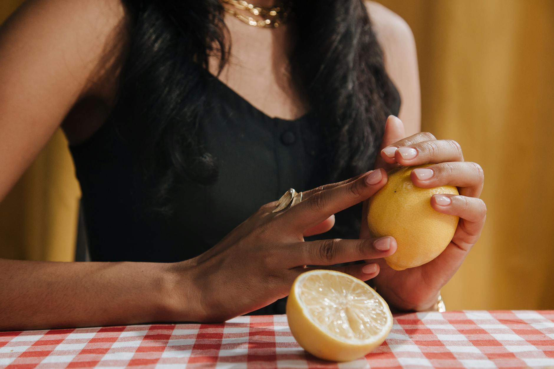 A close-up of a woman holding a fresh lemon at a dining table.