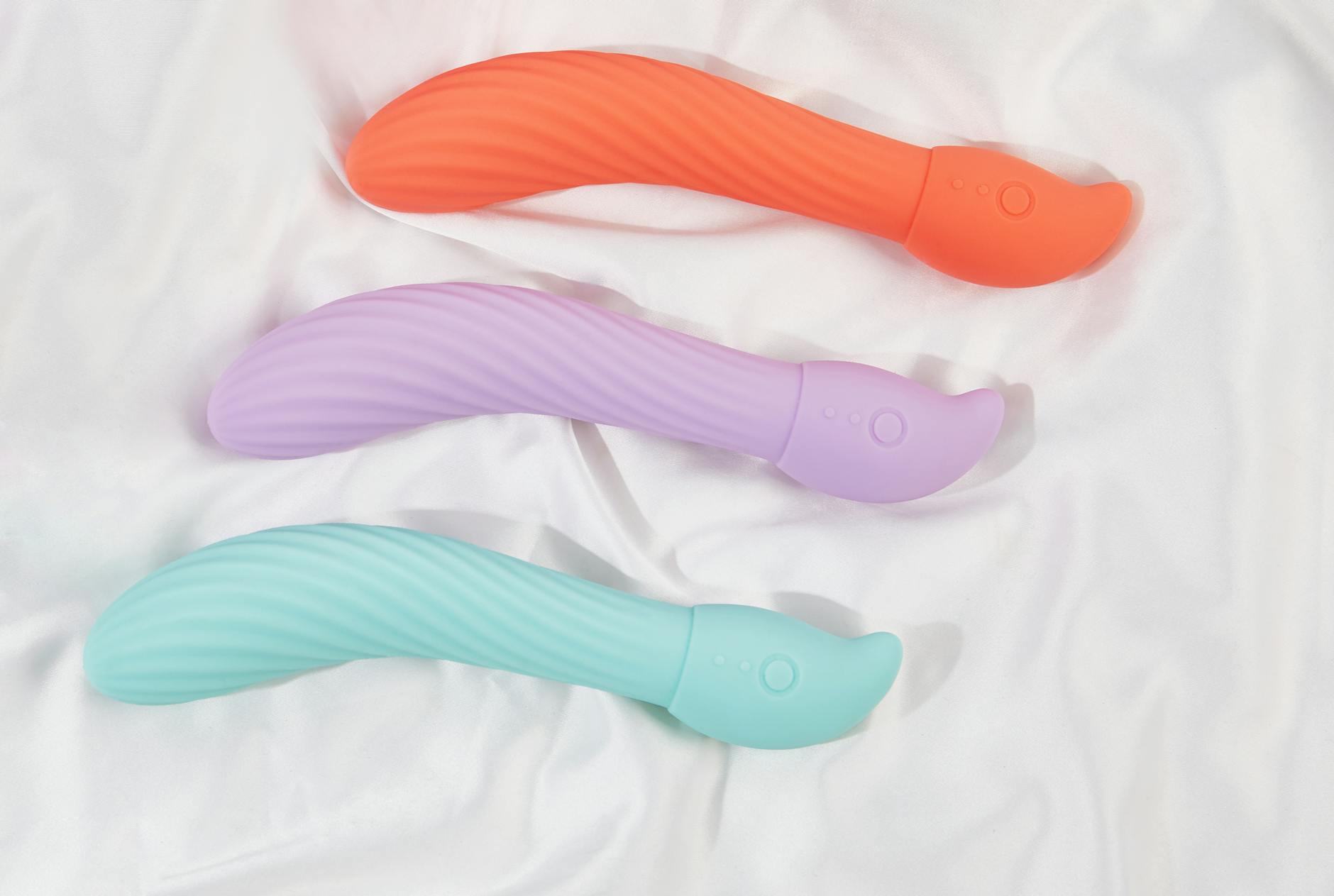 Trois vibromasseurs colorés disposés sur du tissu blanc, mettant en évidence leur texture lisse.