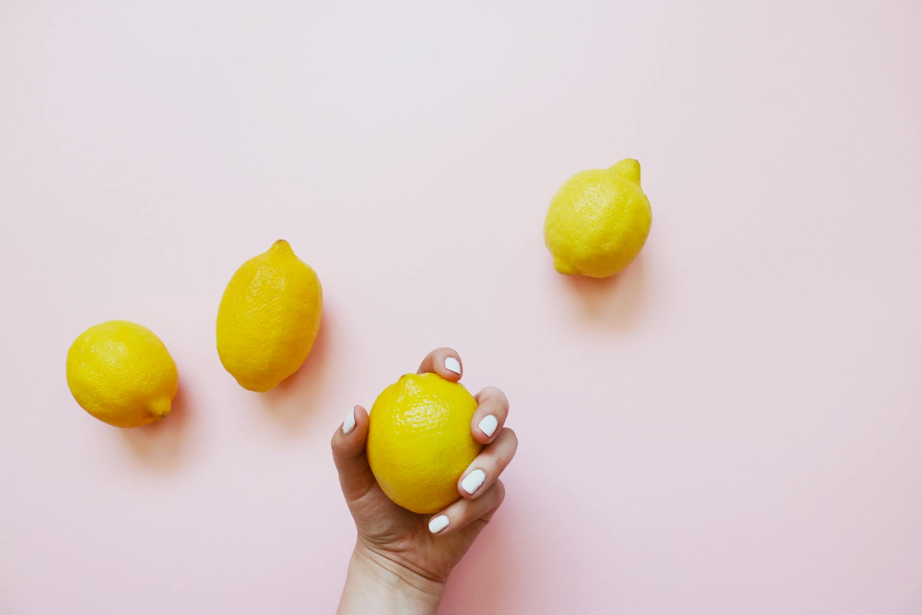 Une main tenant un citron frais sur un fond rose doux, symbole de renouveau et de plaisir naturel