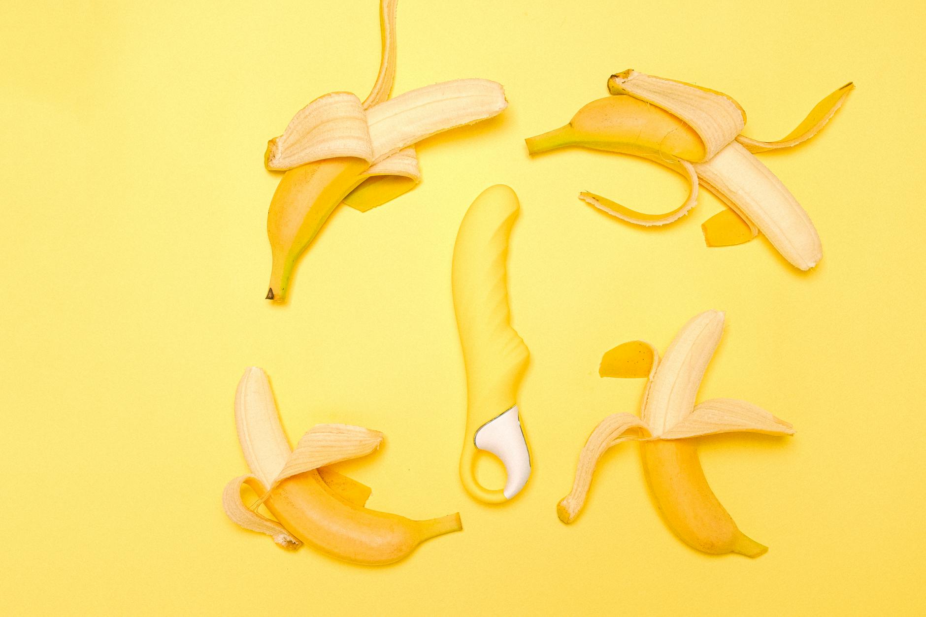 Yellow silicone lemon clitoral vibrator surrounded by fresh lemons on a bright background