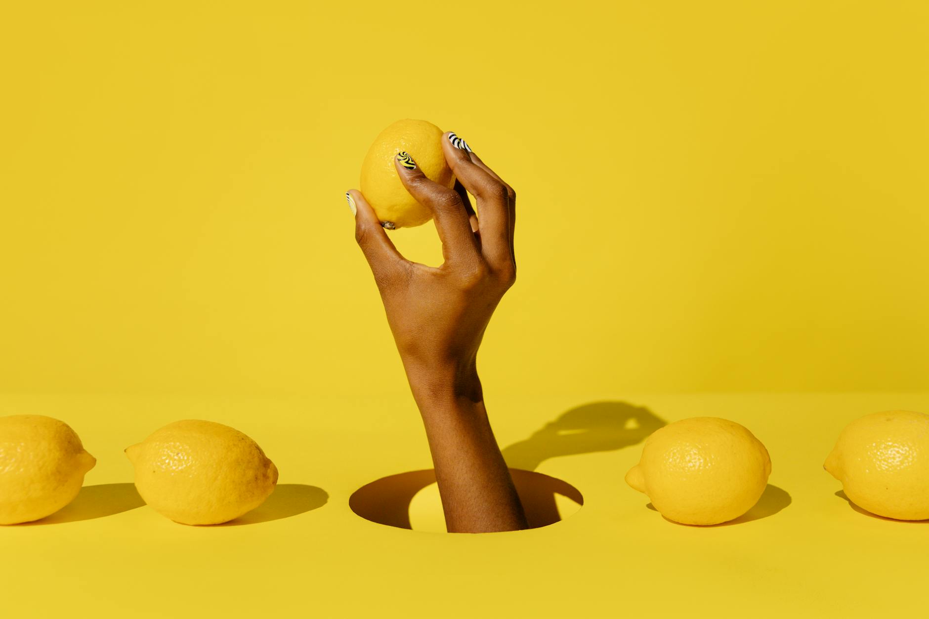 A hand holding a fresh lemon against a vivid yellow background