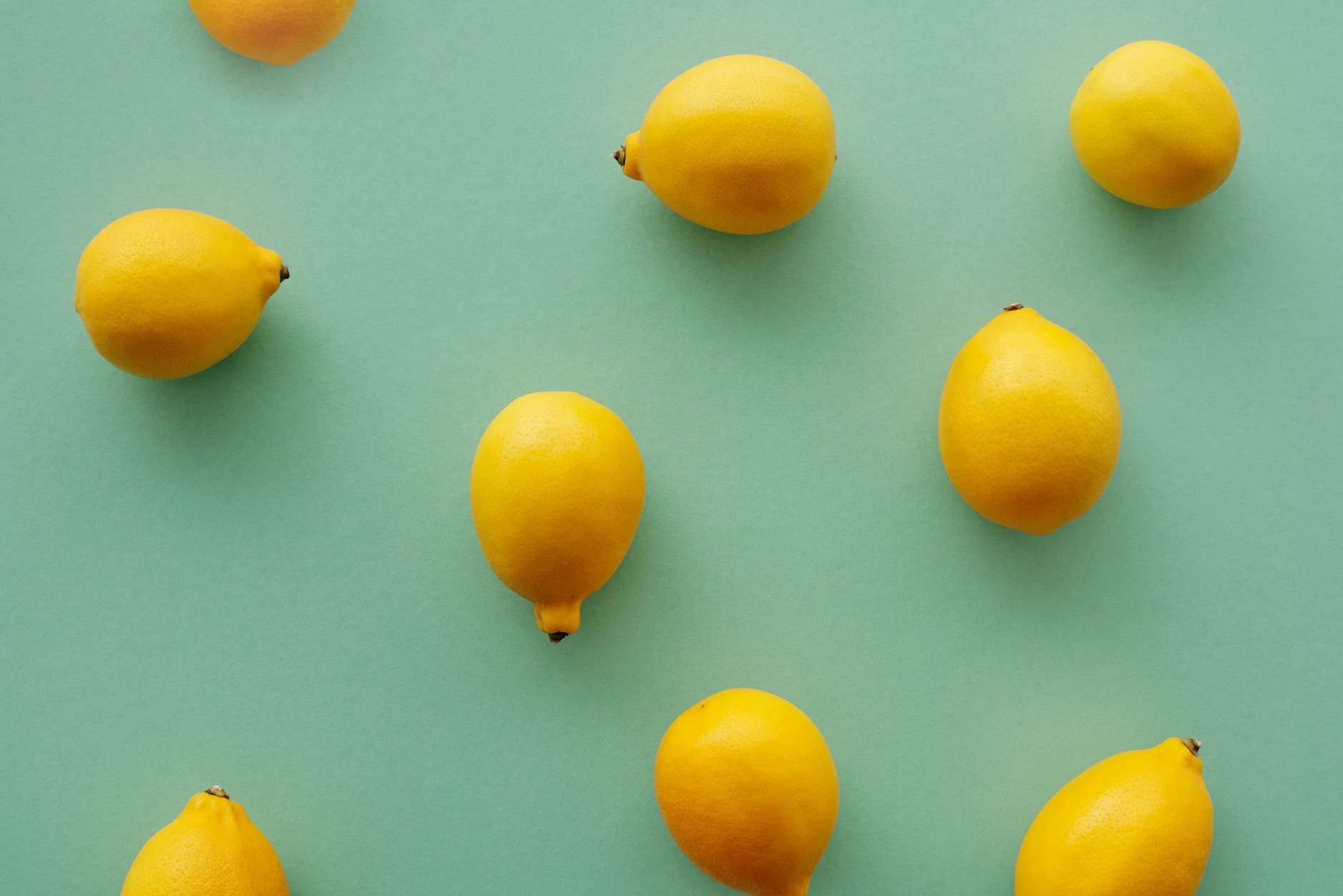 Bright yellow lemons arranged on a pastel green background, creating a fresh and vibrant flat lay composition
