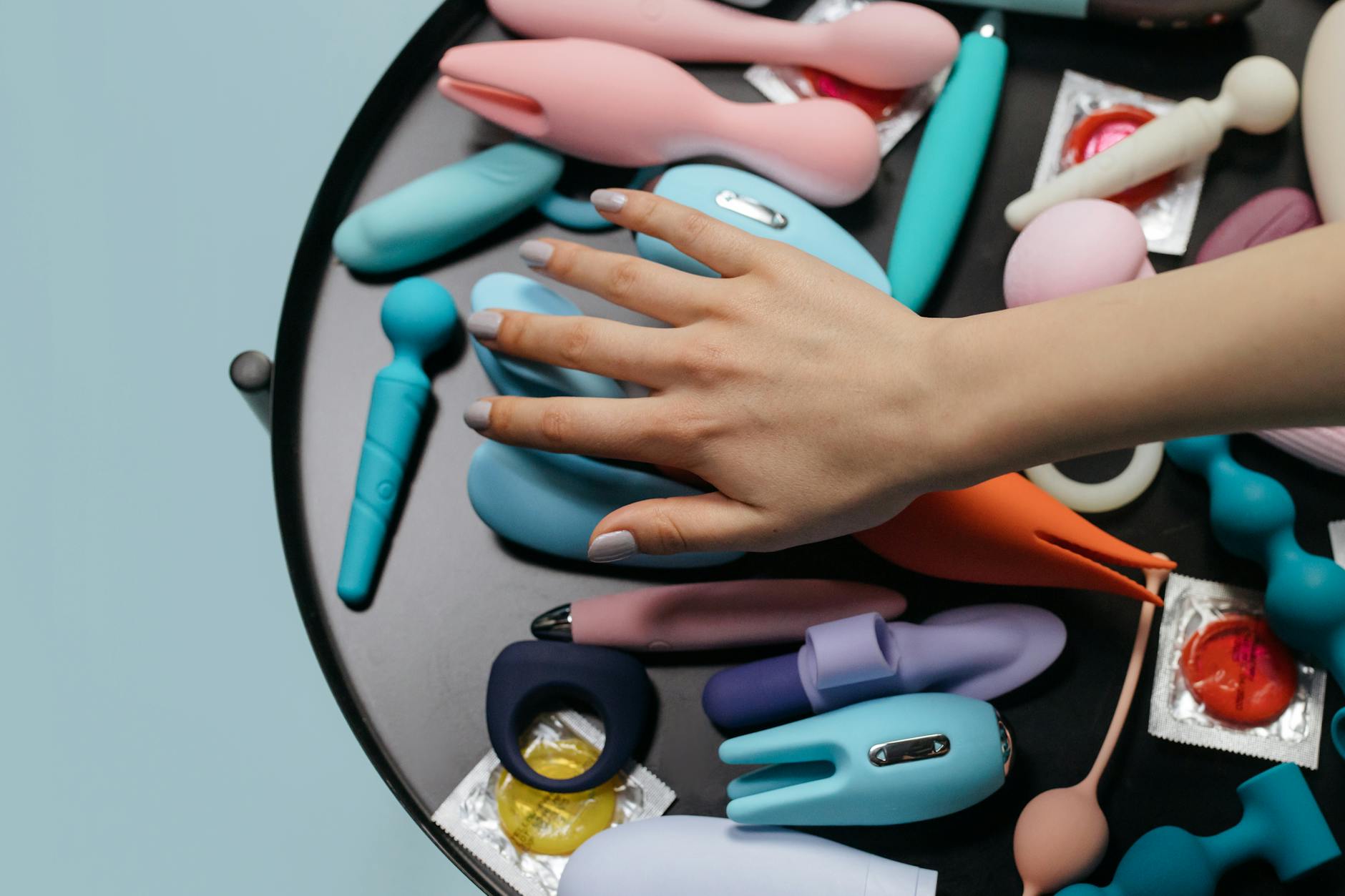 Une main tenant un vibromasseur citron à succion parmi d'autres jouets sexuels colorés sur une table.