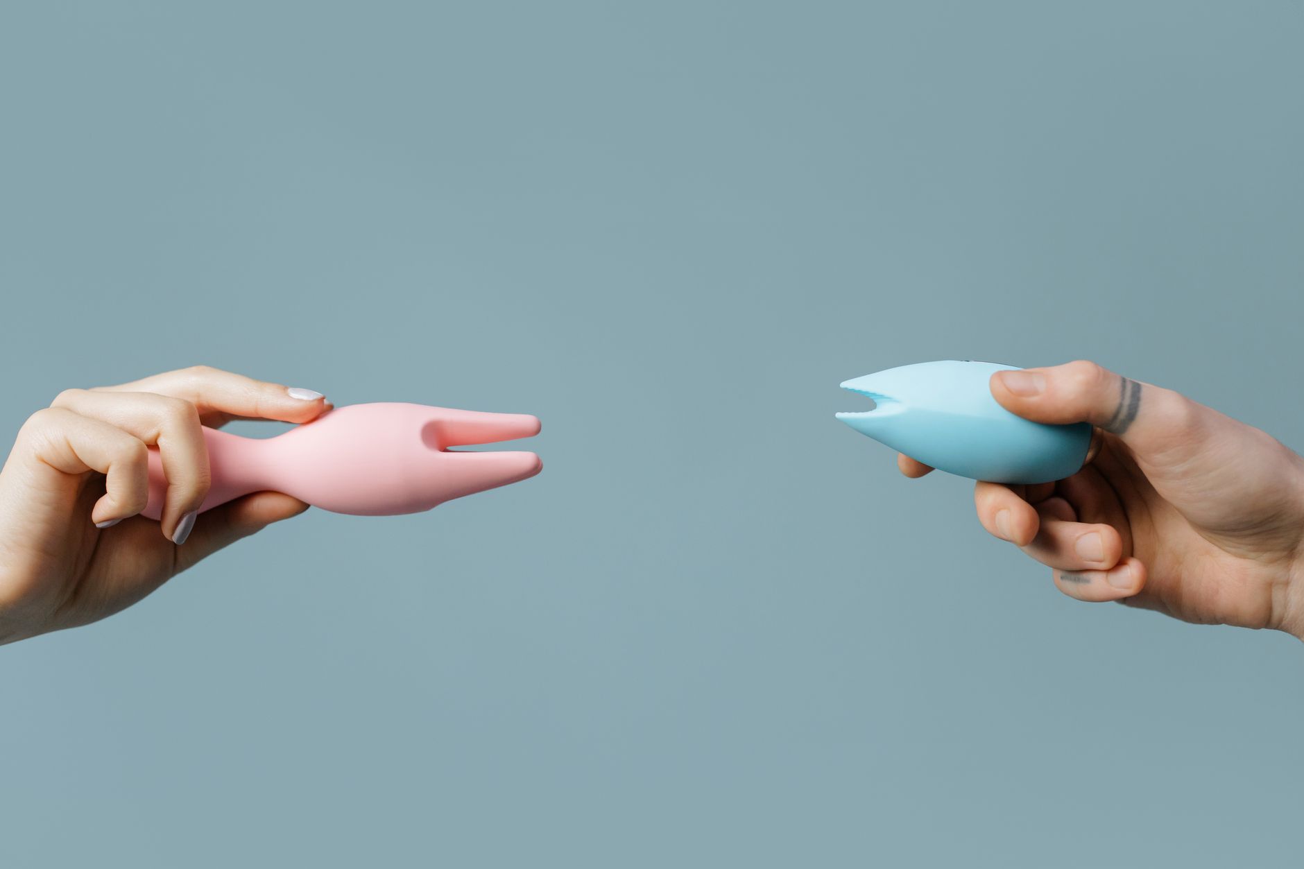 Two hands holding silicone vibrators against a pastel background, representing pleasure exploration during hormonal transitions.
