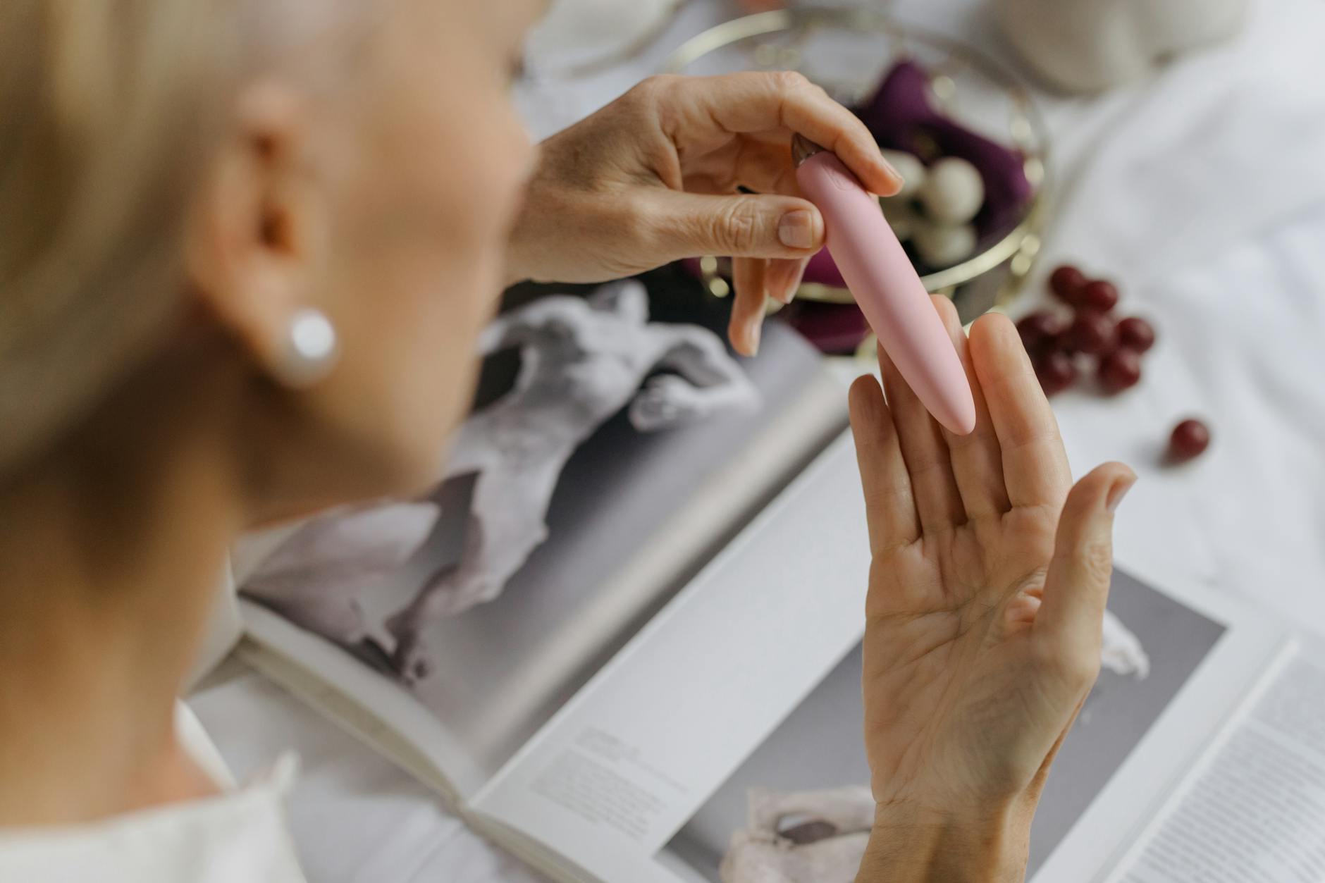 Gros plan d'une femme tenant un vibromasseur rose, avec des livres d'art en arrière-plan