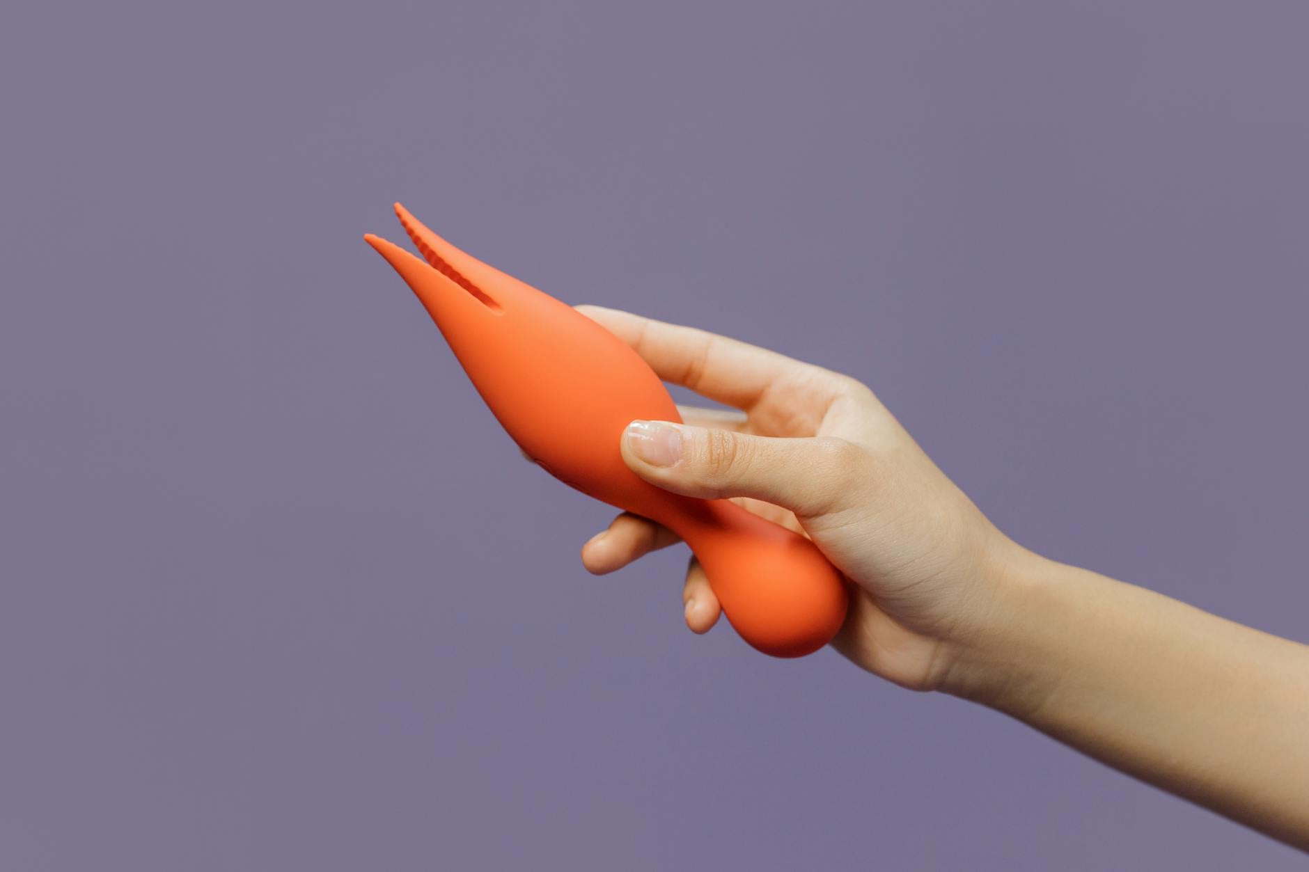 Gros plan d'une main tenant un vibromasseur orange vif sur fond minimimaliste violet, showcasing modern sensuality.