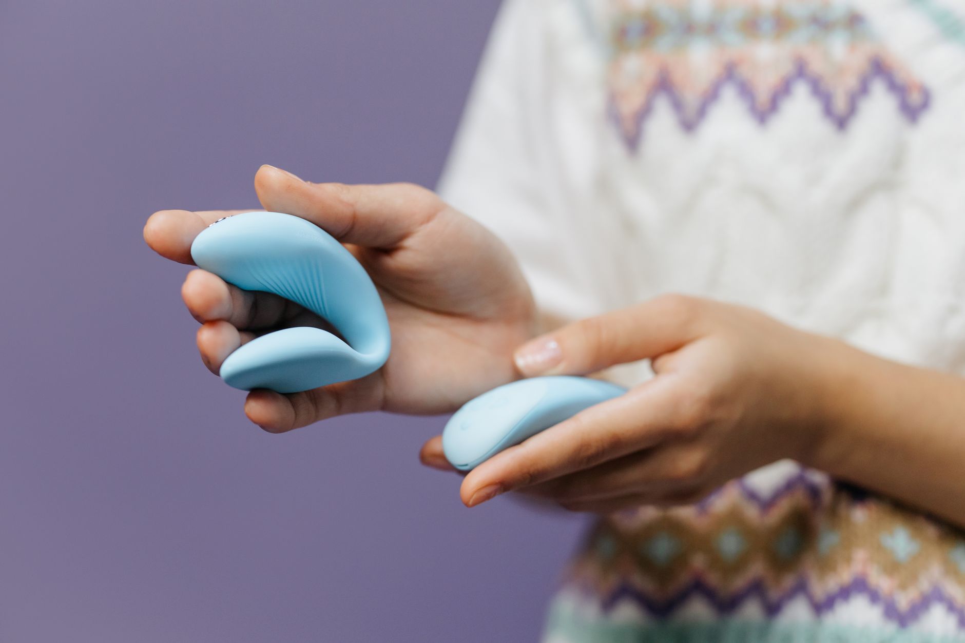 Hand holding a sleek lemon clitoral vibrator against a soft purple background, emphasizing the toy's design and texture