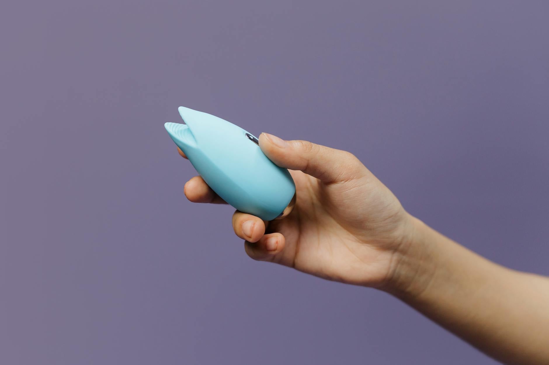 Vibromasseur bleu en silicone tenu à la main sur un fond violet, promouvant l'amour de soi et la sexualité