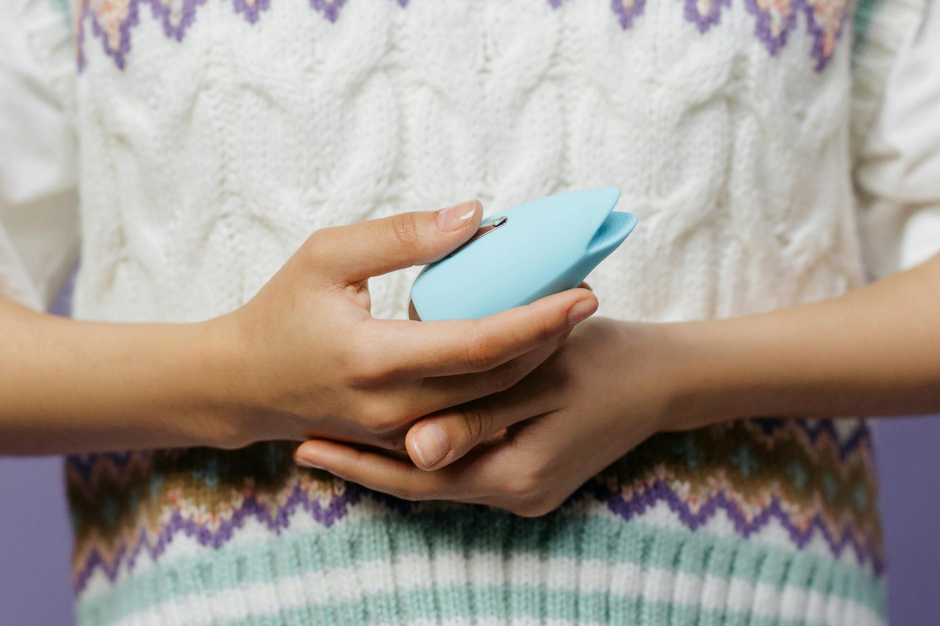 Gros plan des mains tenant un masseur personnel bleu contre un pull tricot.