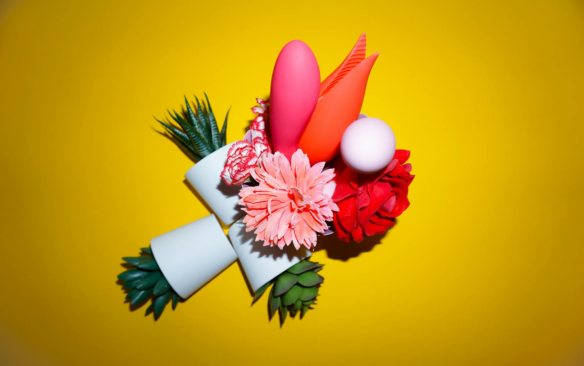 A blue vibrator surrounded by flowers and orange slices on a bright yellow background.